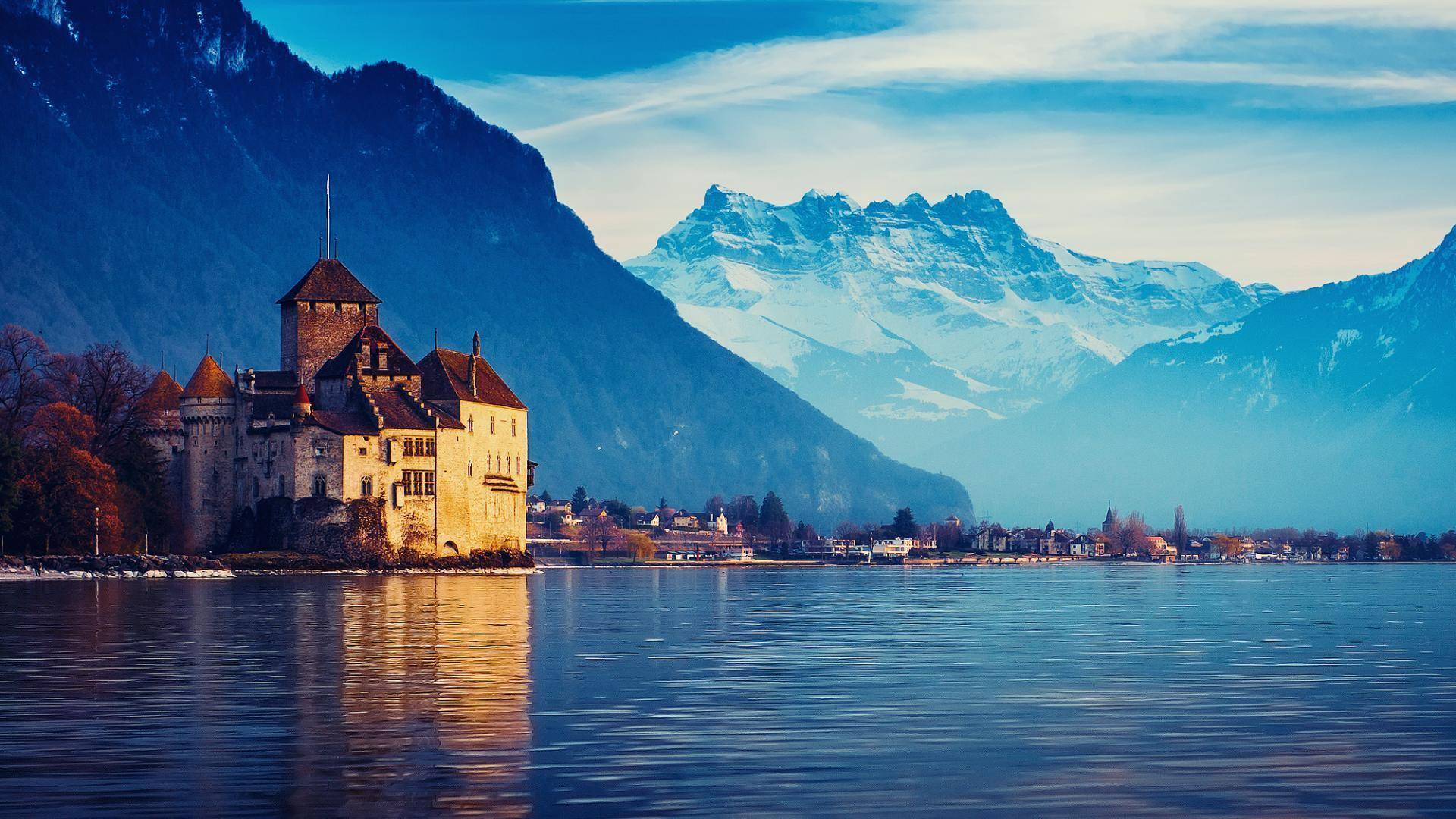 A castle on the shore of a Swiss lake, with snowy mountains rising behind the water